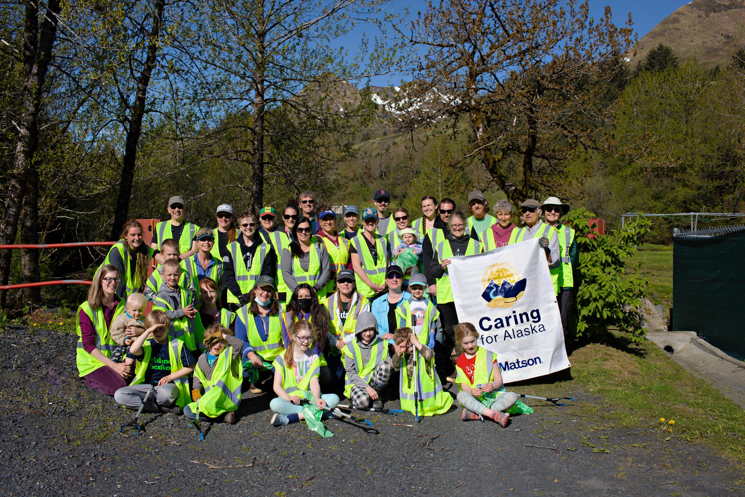 Volunteers wearing their yellow safety vests pose for a group picture with a Caring For Alaska banner.