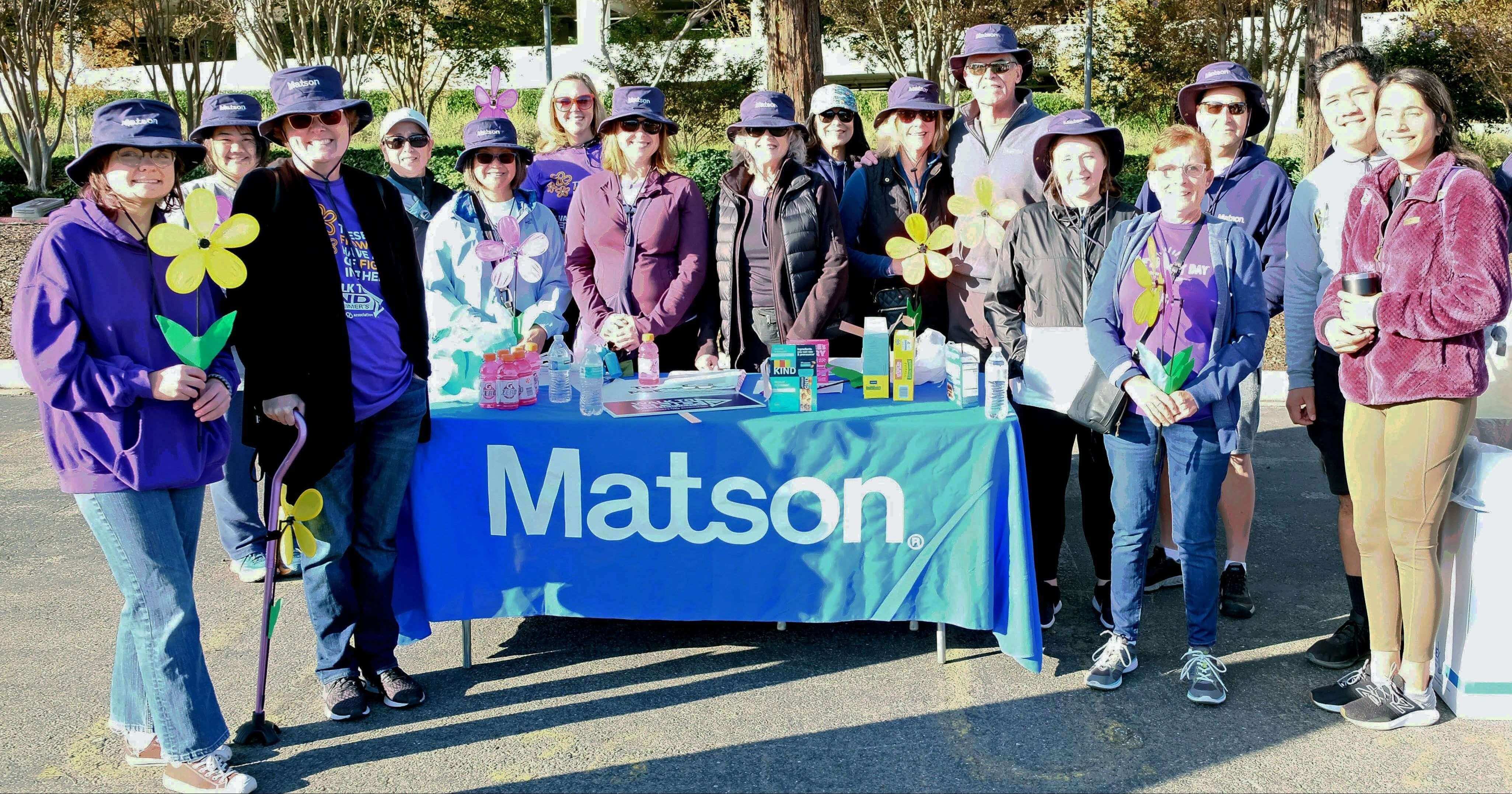 Team Matson holds Alzheimer's Association flowers and poses around a table draped with a Matson tablecloth.