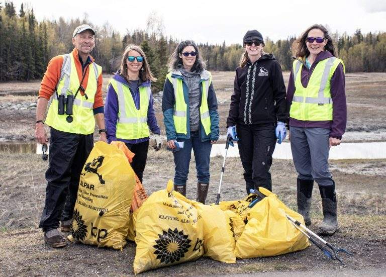 Volunteers post with their grabbers and yellow bags full of trash at an estuary surrounded by trees.