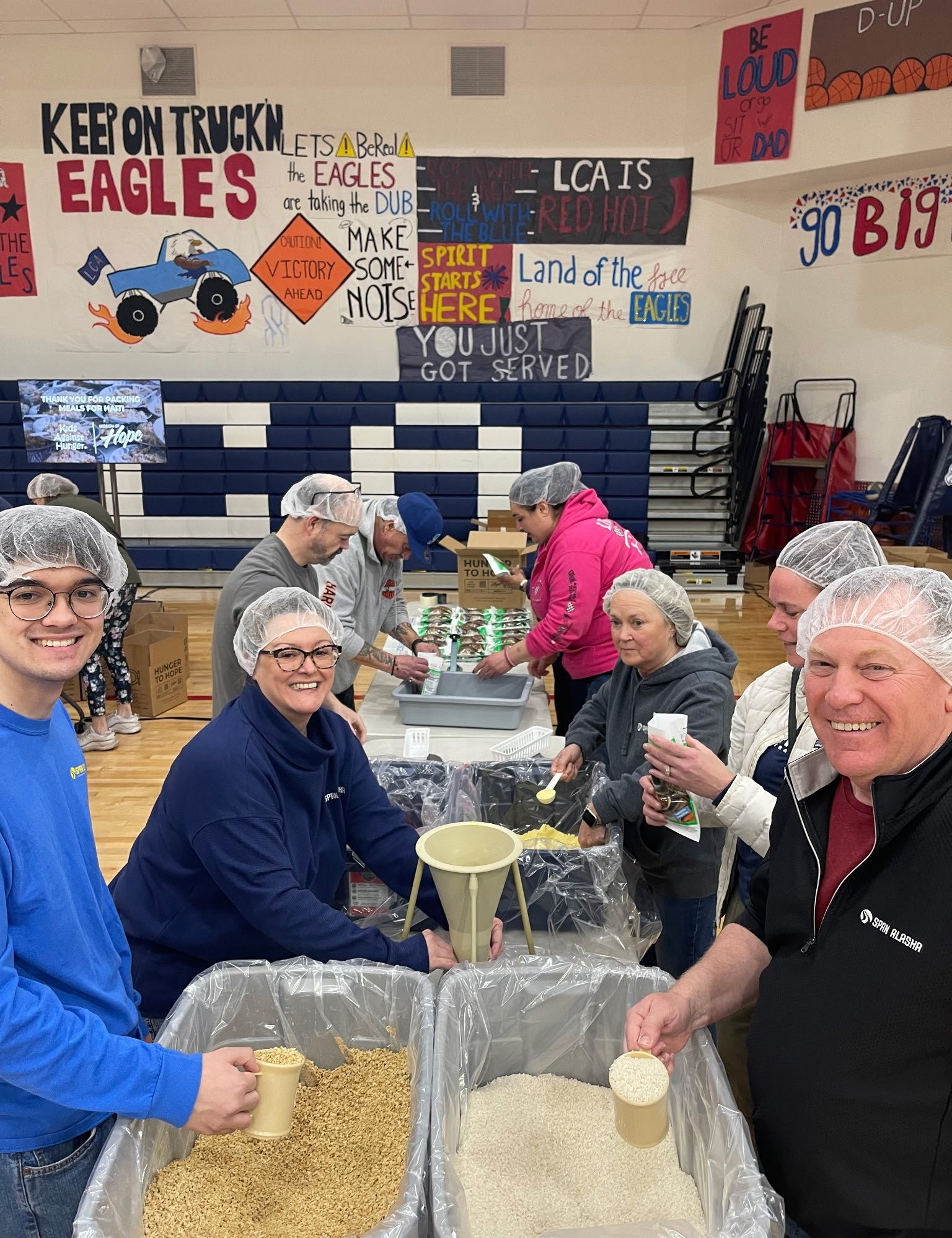 Span employees wearing white hair covers scoop dry goods in a high school gym.